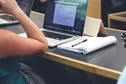 A student sitting at a desk with a laptop open and a notebook, working on an MBA program with no prior work experience.